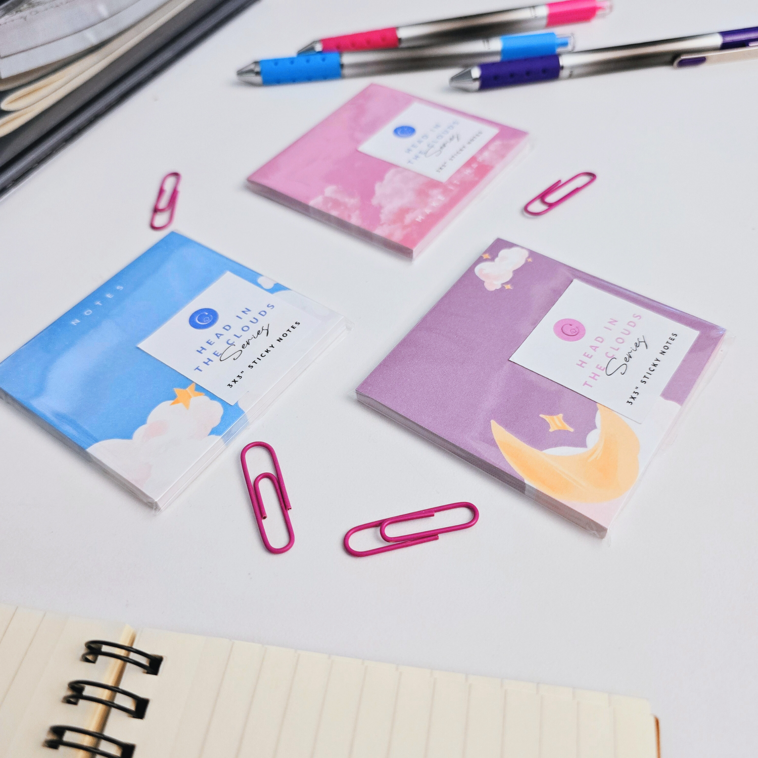 3 cute notepads on a office desk. There are 3 variants: blue, purple, and pink sticky notes. 